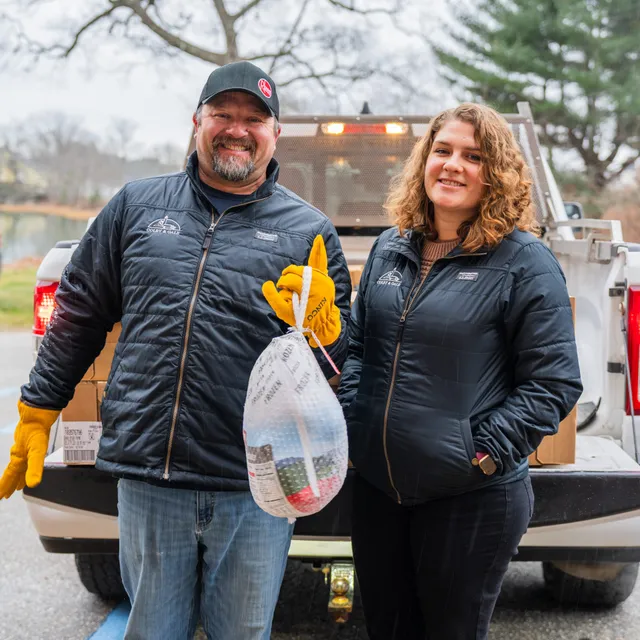 Jackie and Travis holding turkey in front of truck.