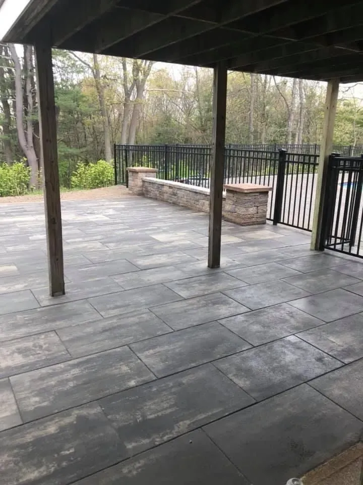 Covered stone patio with dark posts, a built-in bench, and black railing overlooking trees and shrubs
