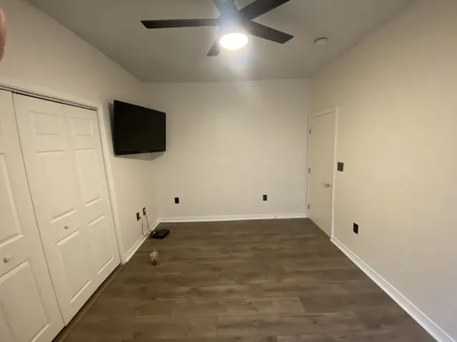 Empty room with wood-look floor, white walls, closet, TV, door, and ceiling fan.