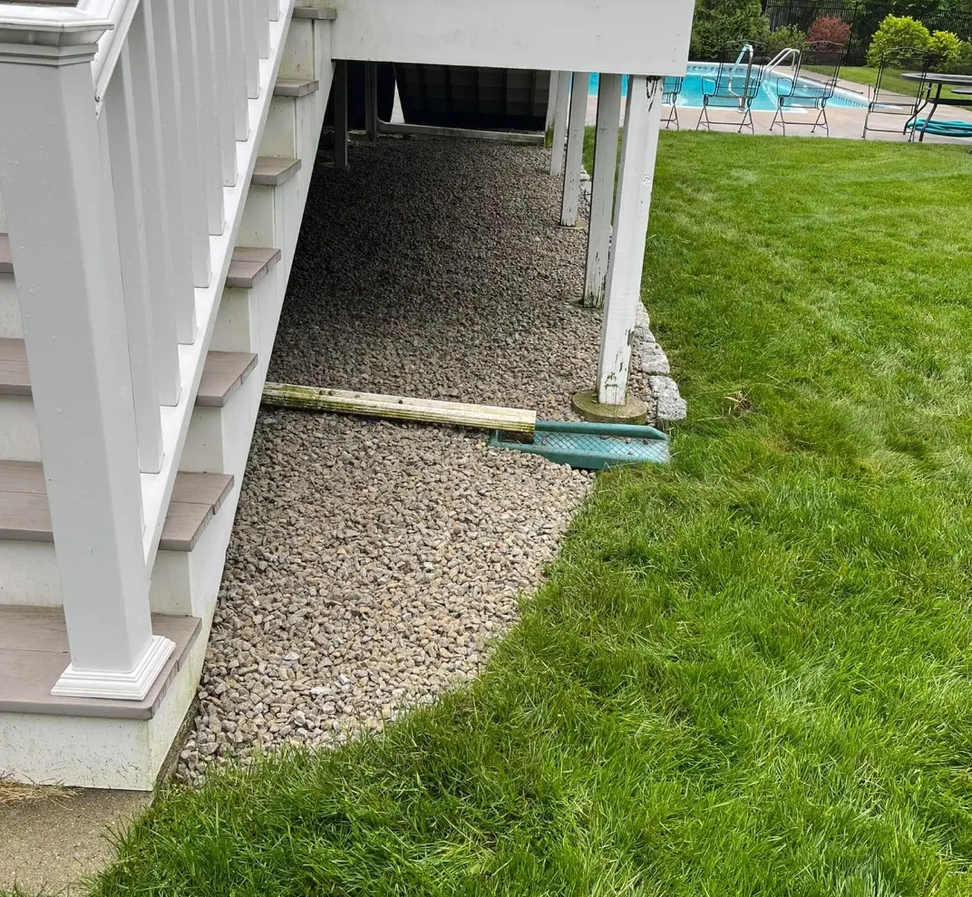 View of a backyard with a deck, stairs, gravel area, and a swimming pool in the background.