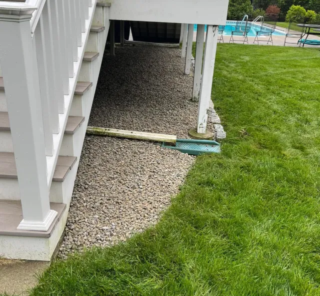 View of a backyard with a deck, stairs, gravel area, and a swimming pool in the background.