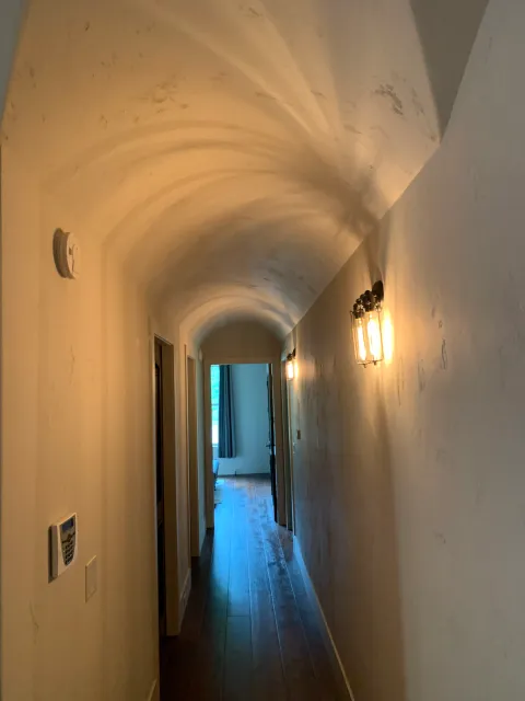 A long hallway with a vaulted ceiling and a light on the wall.