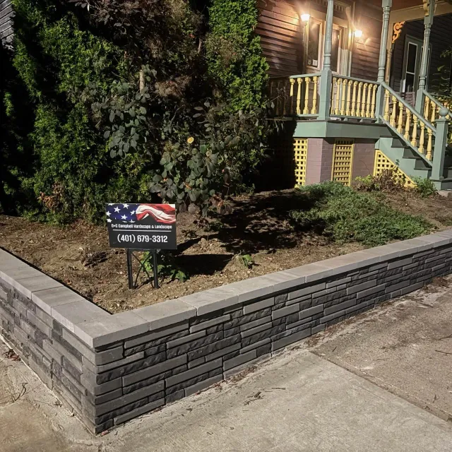 Black retaining wall with stone texture and landscape bed with green shrubs