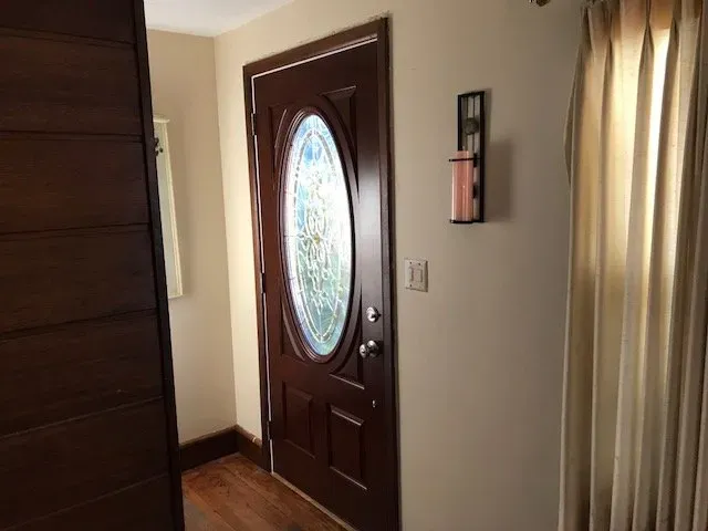 A door with a stained glass window is in a hallway next to a window.