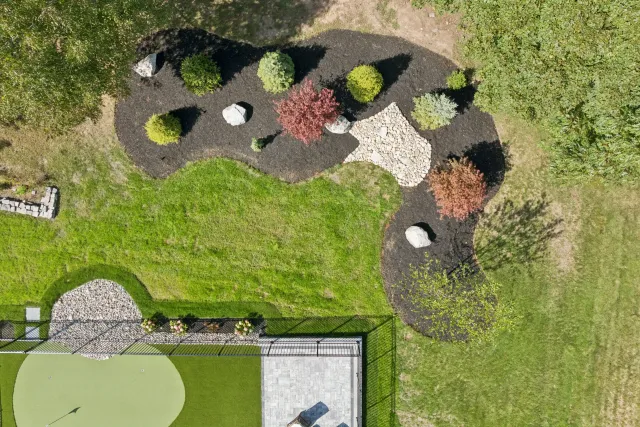 Overhead view of a landscaped area with mulch, plants, rocks, and a putting green surrounded by green grass.