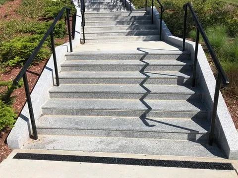 Outdoor stone stairs with black handrails and a zigzag shadow