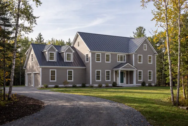 General contractor: taupe-sided colonial with standing seam roof, dormered garage wing and a curved gravel drive