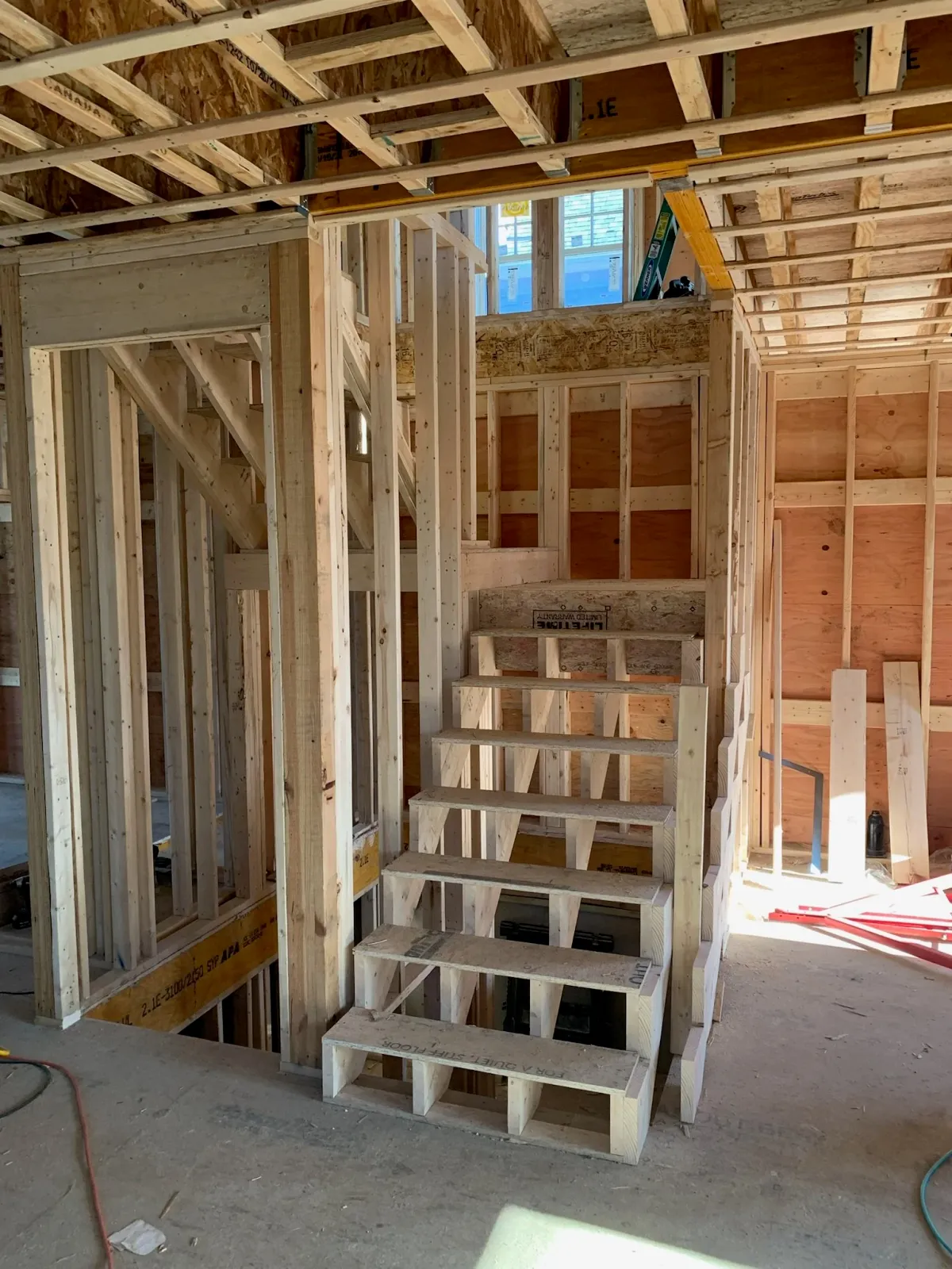Interior view of a house under construction showing wooden framing, stairs, and an unfinished wall with a window. Scituate, Norwell, Hanover, Hanson, Marshfield, South Shore. Massachusetts Local Construction Company.