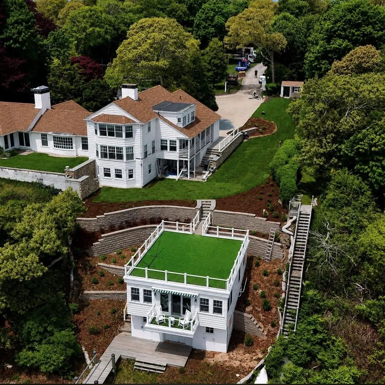 Aerial view of a white house with red roof and green rooftop terrace amid lush trees and landscaped slopes