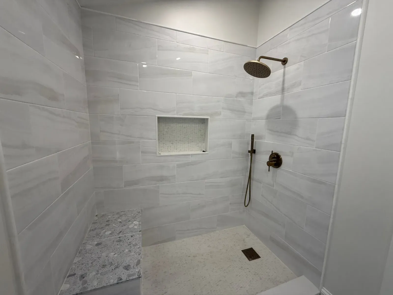 Tiled shower stall with bronze fixtures, a built-in bench, and a recessed shelf.