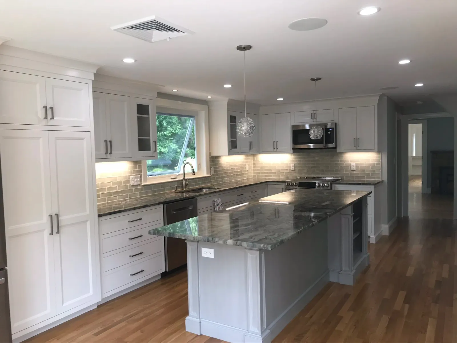 Modern kitchen with white cabinets, gray countertops, a marble island, stainless steel appliances, wood flooring, and a window above the sink.