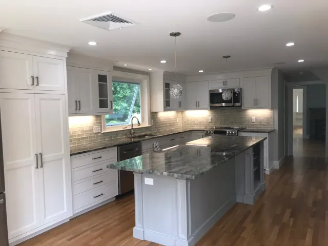 Modern kitchen with white cabinets, gray countertops, a marble island, stainless steel appliances, wood flooring, and a window above the sink.