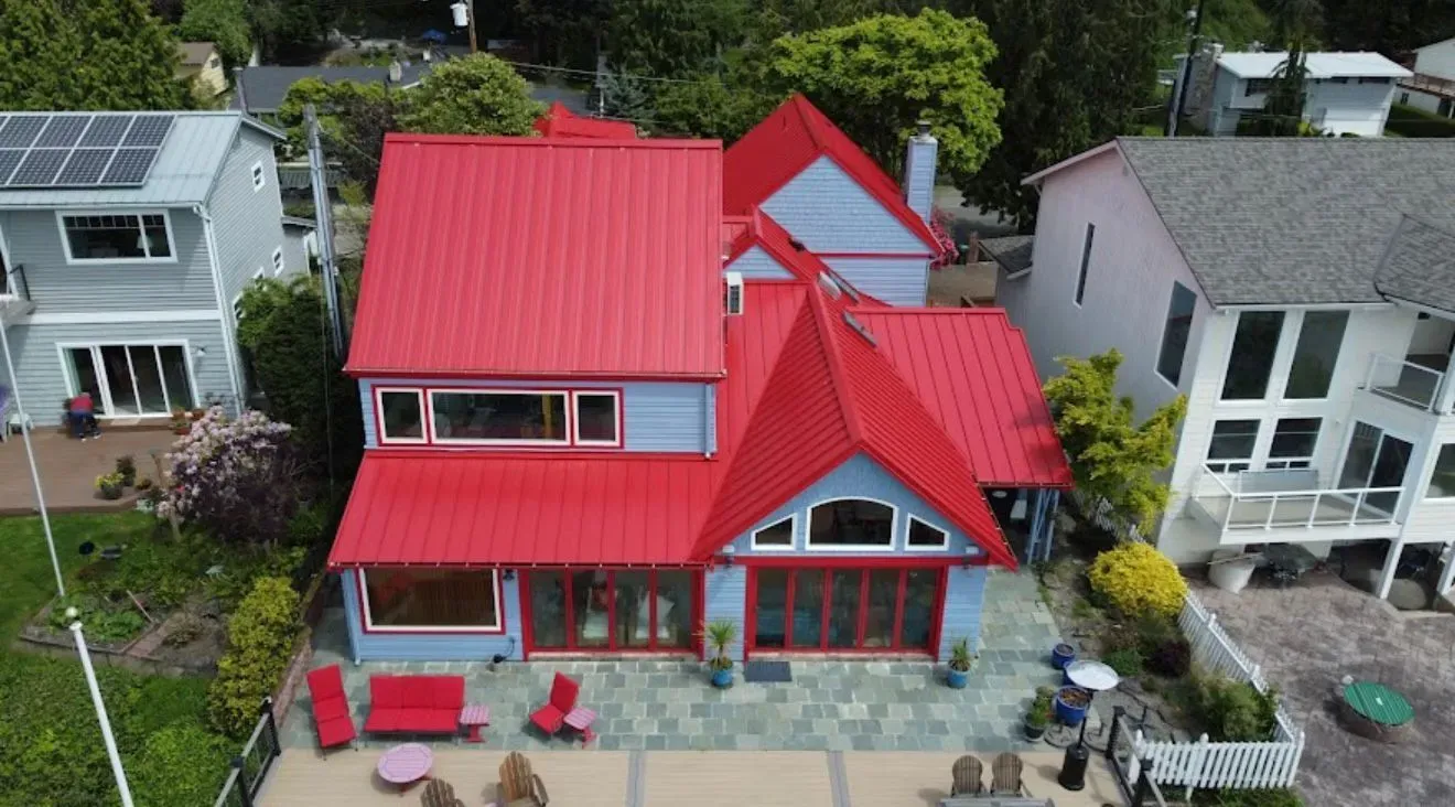 Blue house with red metal roof, patio furniture, and waterfront view.