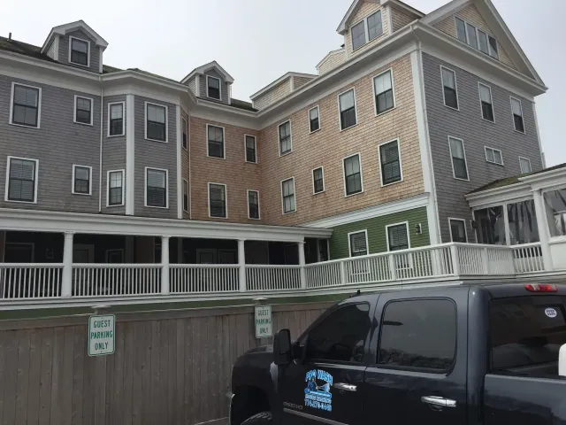 A multi-story building with gray and tan siding. A pickup truck is in front. Cloudy sky.