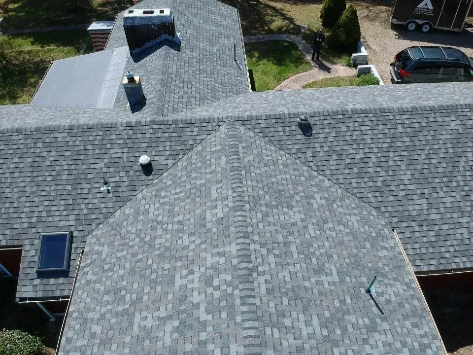 Aerial view of gray shingled house roof with skylights and parked cars nearby.