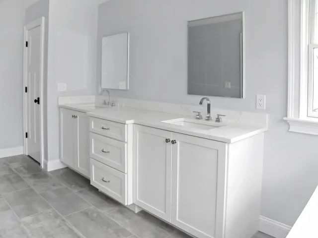 White double vanity in a bathroom with gray walls, mirrors, and a door.