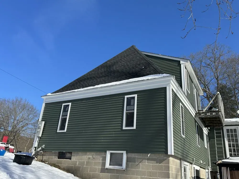 Green house with dark roof and white trim on a snowy day under a clear blue sky