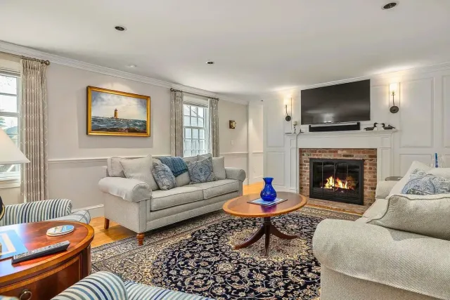 Wood staircase with white railing in a bright hallway.Living room with fireplace, two sofas, and a navy rug.