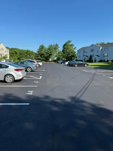 An outdoor residential parking lot on a sunny day with cars parked along both sides under a clear blue sky.
