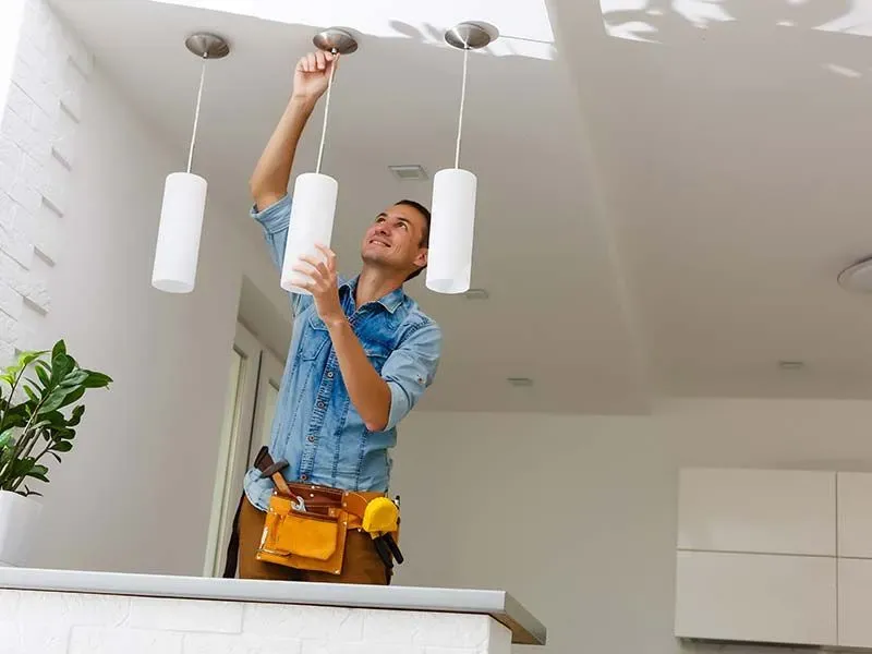 A man is hanging a light from the ceiling in a kitchen.