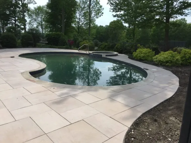 A large swimming pool is surrounded by a patio and trees.