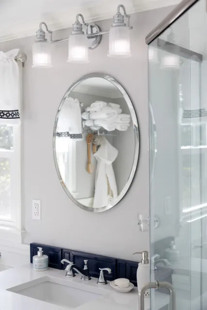 A modern bathroom vanity with a white countertop, dark blue tiled backsplash, oval mirror, and three glass pendant lights.