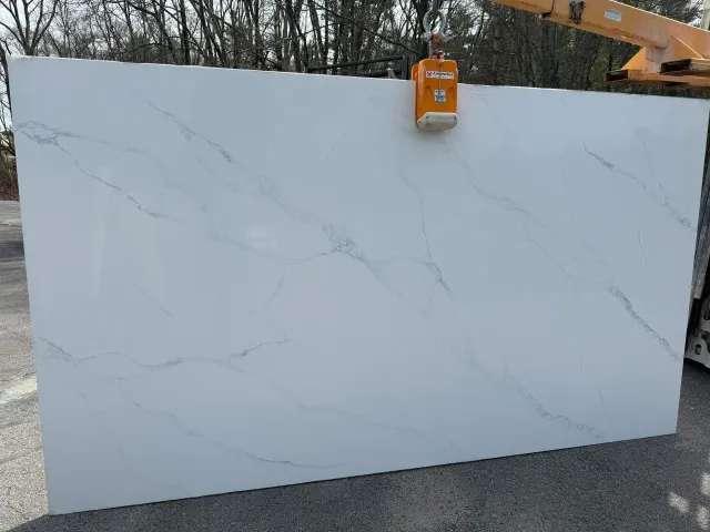 A large white granite slab is being lifted by a crane.