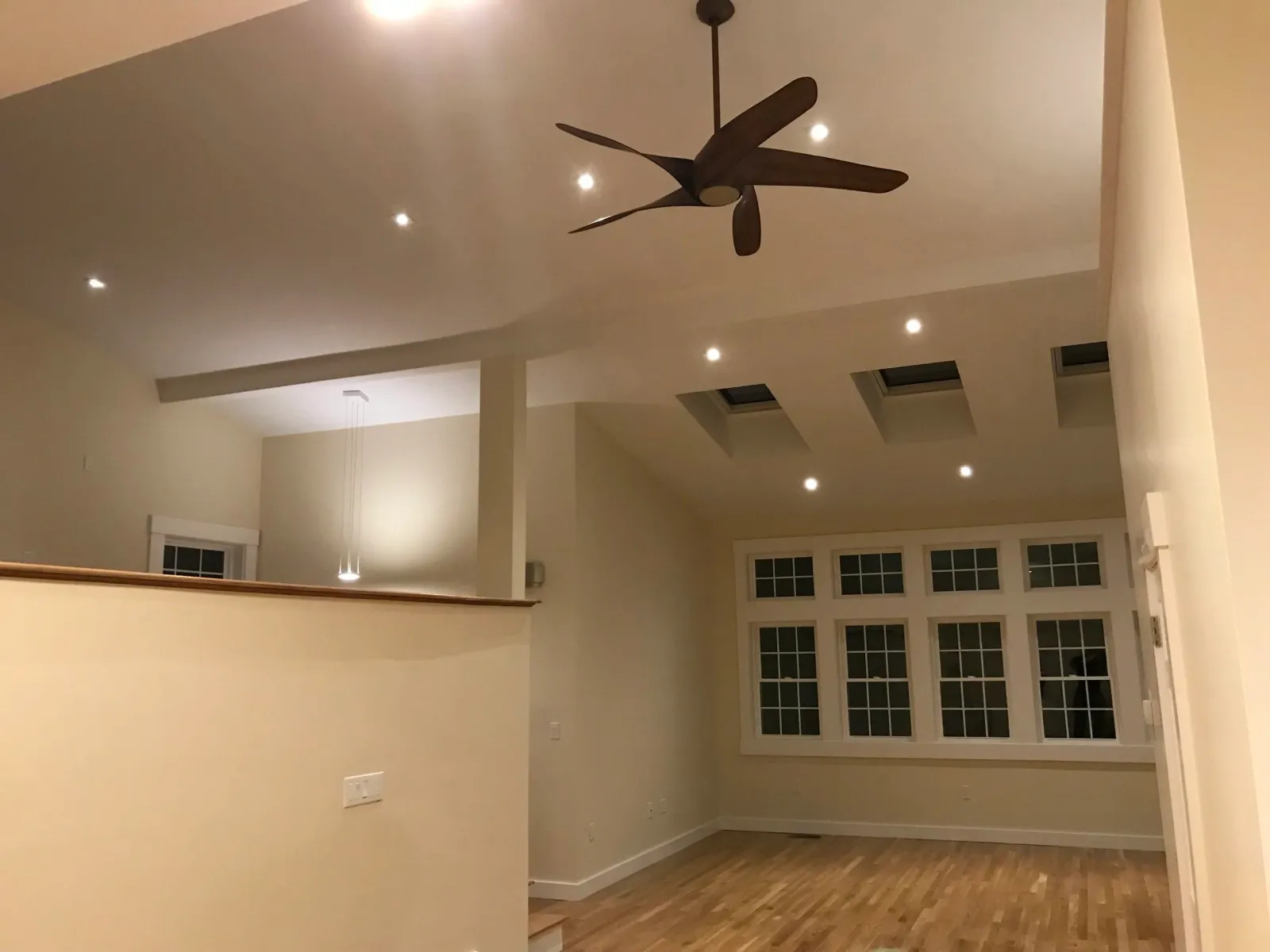 Modern interior with high ceiling, skylights, large windows, ceiling fan, and wooden floor.