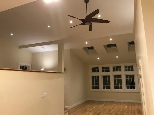 Modern interior with high ceiling, skylights, large windows, ceiling fan, and wooden floor.