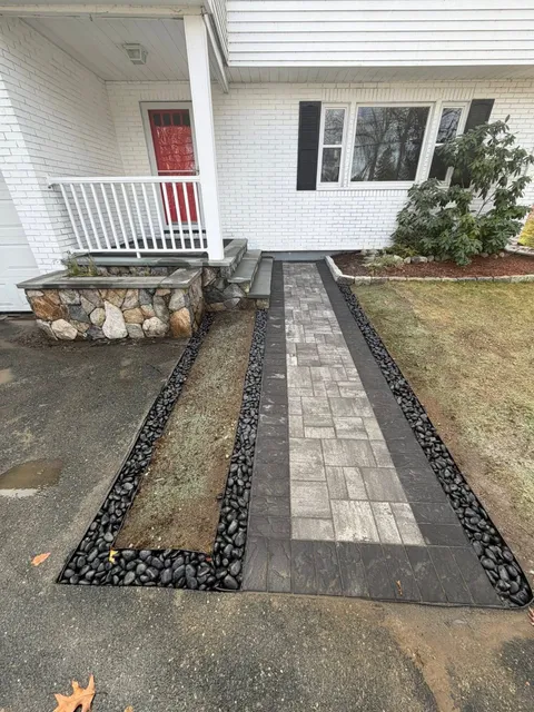 Front walkway with central stone path, bordered by gravel and mulch, leading to a porch with white railing and red door