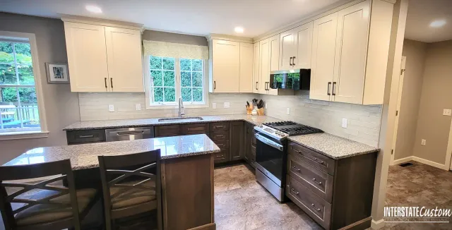 Wilbraham, MA kitchen remodel showcasing two-tone cabinetry with cream uppers and dark wood lowers, granite countertops, a subway tile backsplash, and a central island.