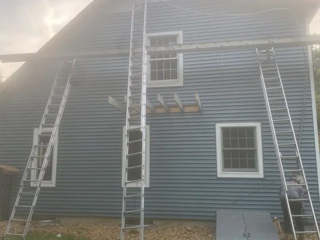 House exterior with blue siding and two ladders leaning against the wall under a steep roof.