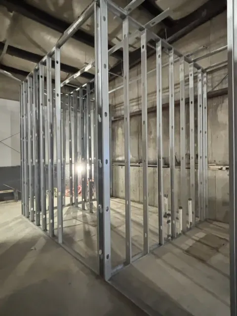 Unfinished building interior with metal wall studs and concrete floors under exposed ceiling beams