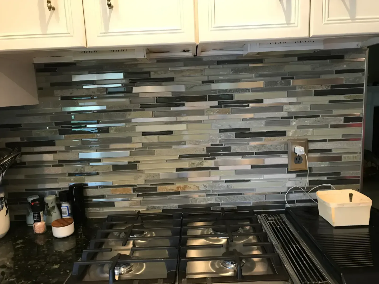 Kitchen stove with stainless burners and a gray tile backsplash under white cabinets