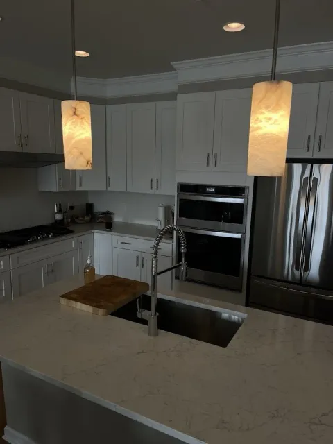 dual marbled, cylindrical pendant lights installed above a kitchen island and recessed lighting expertly spaced in kitchen