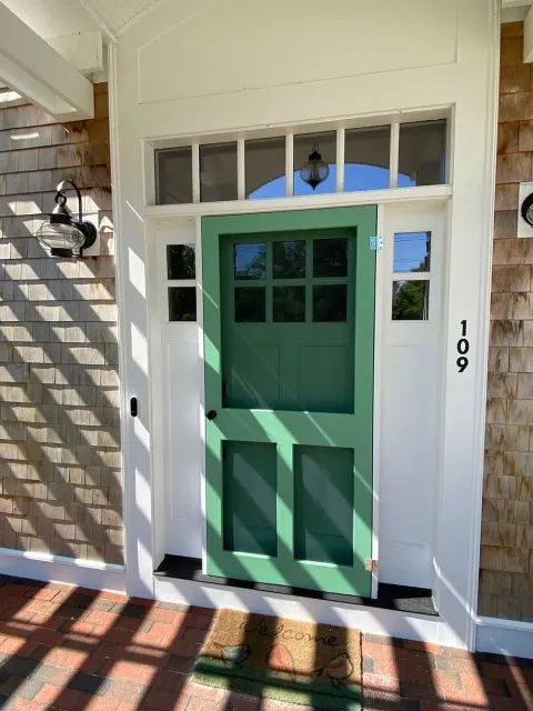 Green front door with windows and white trim at house number 109, beside a brick walkway.
