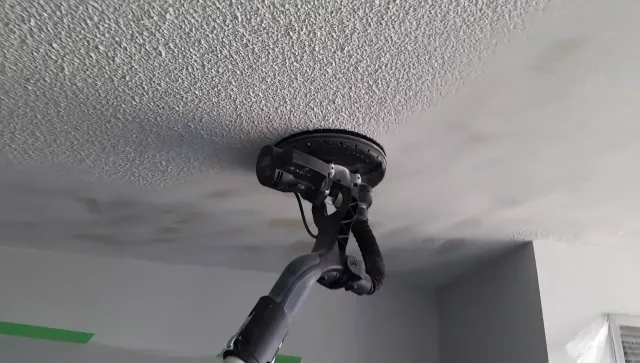 A person sanding a textured ceiling with a long-handled sander.
