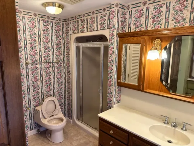 A bathroom with a toilet , sink , mirror and shower.