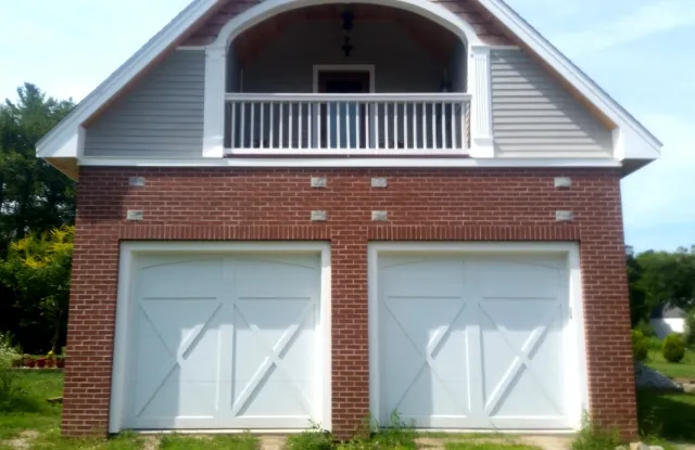 Two-car garage with brick base, white doors, and a balcony above, under a light gray roof.