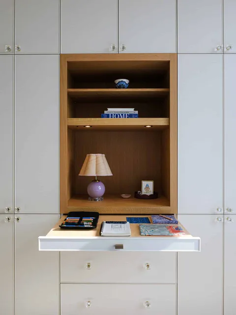 Built-in cabinetry nook with open shelving, a table lamp, and a pull-out desk