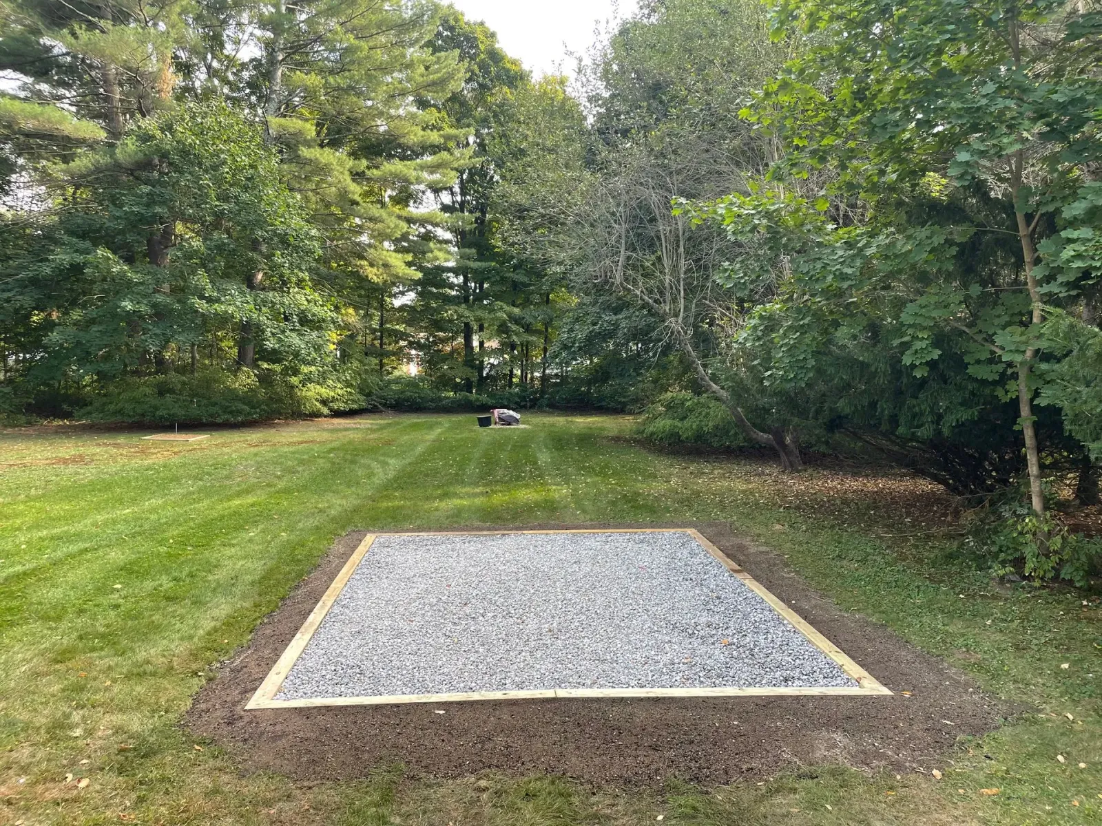 Gravel-filled square bordered with wood in a grassy yard, with trees in the background.