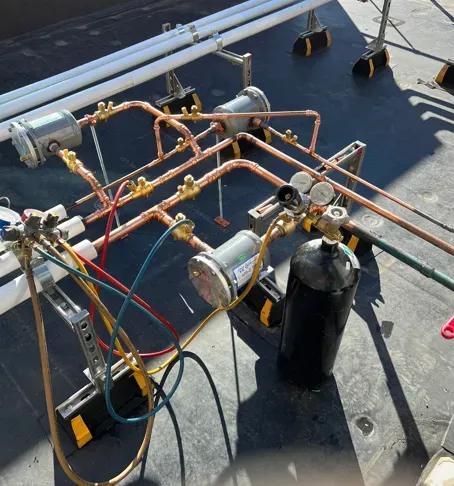 Copper pipe and gas cylinder setup on a rooftop, with gauges and hoses connected to equipment