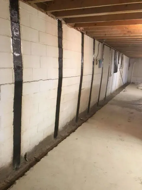 Unfinished basement wall with concrete block and wood framing along a narrow corridor