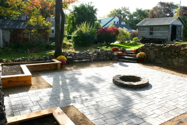 The foundation from a long-gone barn becomes an outdoor gathering area with built-in fire pit. We added natural stone stairs in one corner to easily access the house. Corner raised beds for growing flowers and vegetables help frame the design and pr…