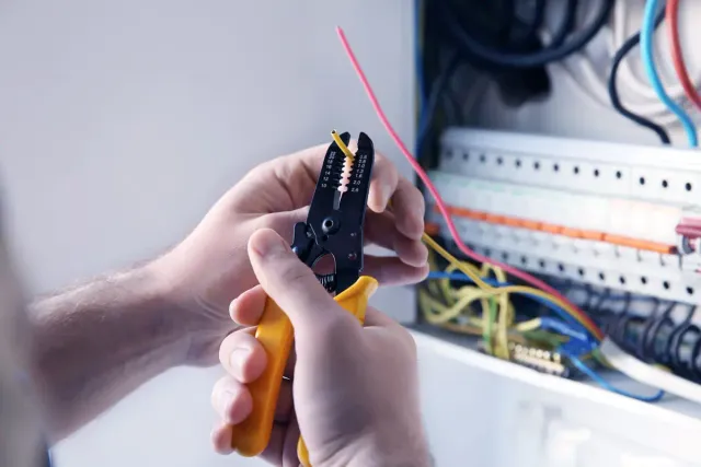 Electrician stripping wire at an open breaker panel during a service upgrade