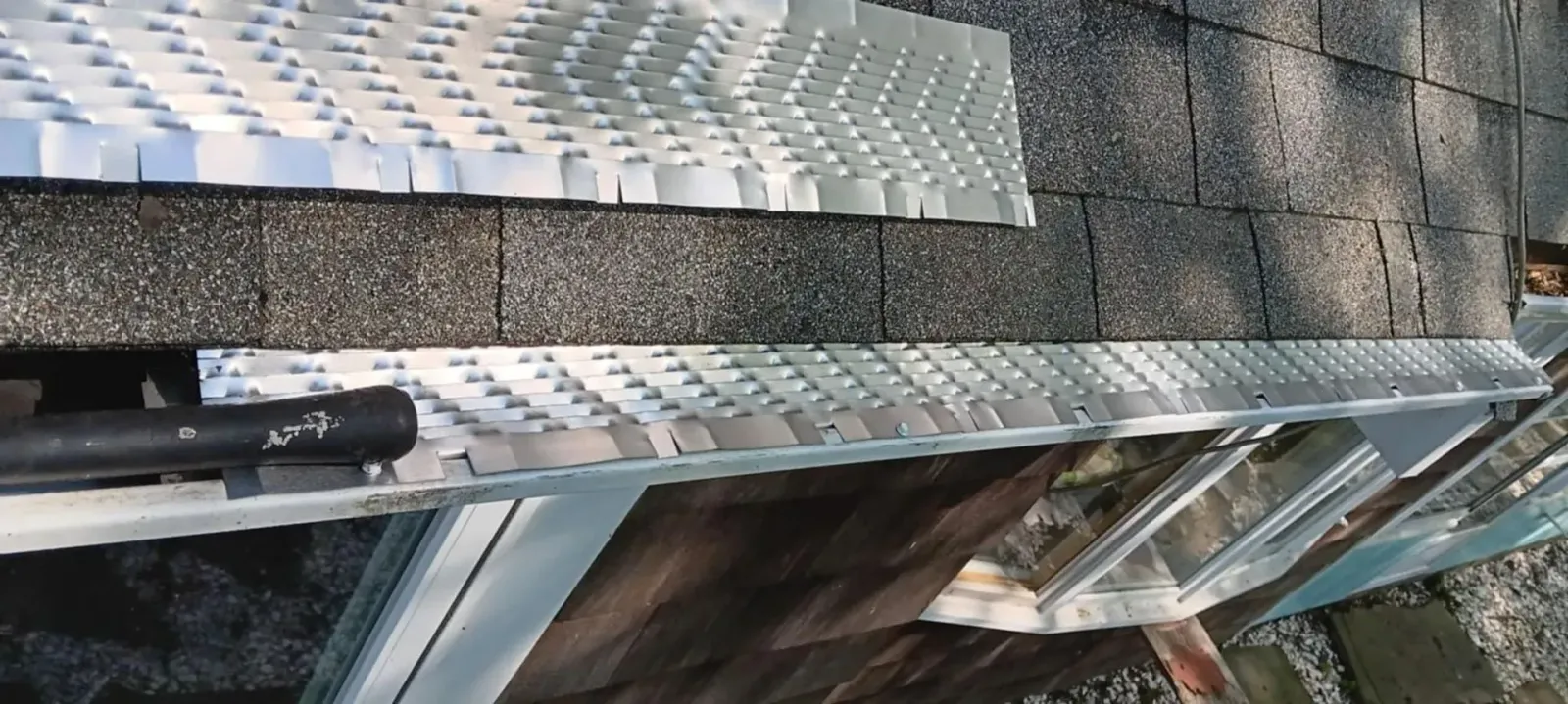 Close-up of gray roofing shingles and flashing on a sloped roof, with a patch of snow nearby
