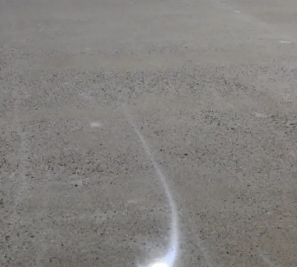 A bright, curved streak of light on a sandy surface, possibly a reflection or a light trail.