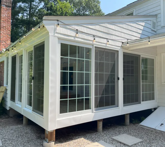 White sunroom enclosure with sliding windows installed on residential home