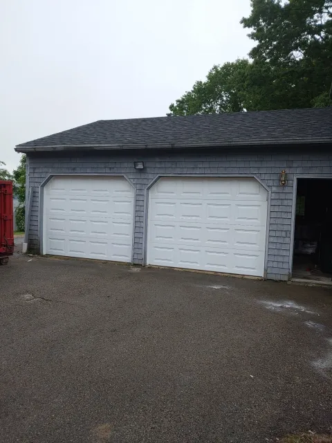 Gray garage with two white garage doors and gravel driveway.
