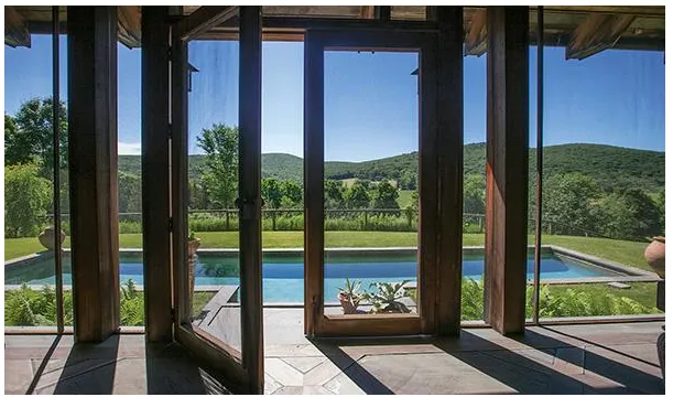 View of a swimming pool and green landscape through open glass doors